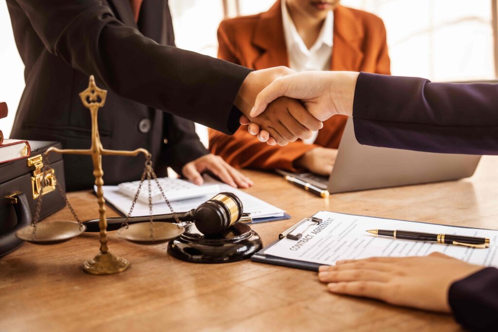 Lawyers shaking hands after successful contract agreement with gavel and scales of justice on desk. Lawyers shaking hands after successful contract agreement with gavel and scales of justice on desk.