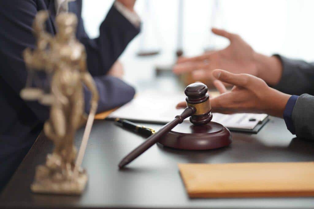 Lawyer and client discussing a legal case at a desk with a gavel and Lady Justice statue in the foreground. Lawyer and client discussing a legal case at a desk with a gavel and Lady Justice statue in the foreground.